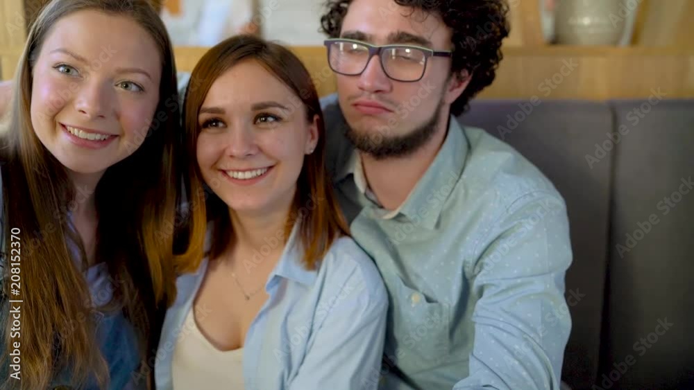 Three friends sit in a cafe, have fun communicating and make selfie. Slow motion Three friends sit in a cafe, have fun communicating and make selfie. Slow motion