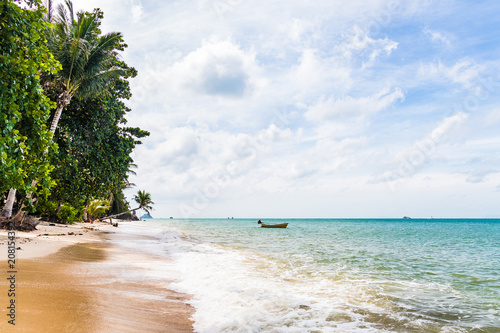 Fototapeta Naklejka Na Ścianę i Meble -  Tropical sandy beach with palms and a wooden boat in the background and blue ocean in the foreground during a bright sunny day, Haad Yao Beach, Koh Phangan, Thailand