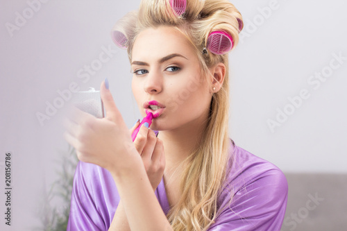 Attractive lady getting make up done.Portrait of beautiful hot blond woman with hair curled putting on bright vibrant pink lip colour in front of pocket mirror.