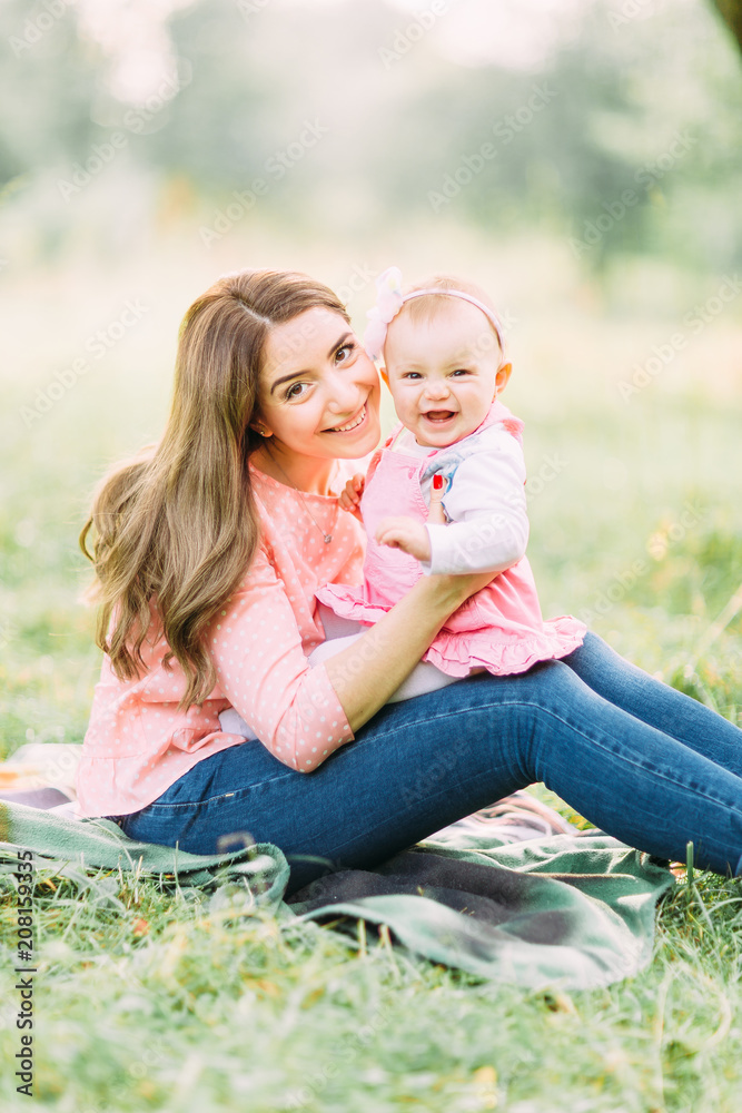 Happy mother and daughter in the park. Beauty nature scene with family outdoor lifestyle. Happy family resting together on the green grass, having fun outdoor. Happiness and harmony in family life. Happy mother and daughter in the park. Beauty nature scene with family outdoor lifestyle. Happy family resting together on the green grass, having fun outdoor. Happiness and harmony in family life.