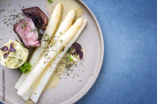 Modern barbecue dry aged sliced fillet steak with white asparagus in butter sauce and mashed potatoes as top view on a plate with copy space right