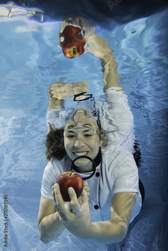 Young female chef inspecting a red apple with a magnifying glass underwater photo