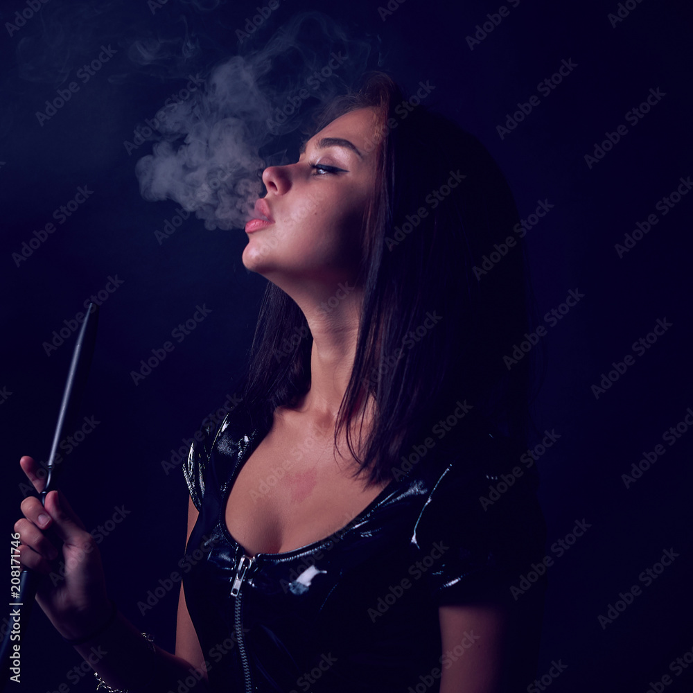 The portret of Young, beautiful girl smokes a hookah or shisha or kalian.  Smoke and passion. Leather or latex dress, sexy outfit.The pleasure of  smoking. Stock Photo | Adobe Stock