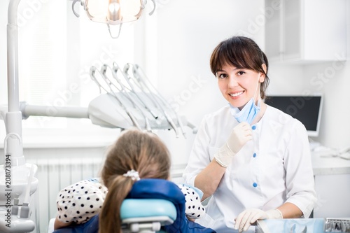 Dentist Smiling Looking at the Camera Next to the Patient Sitting in the Dental Chair