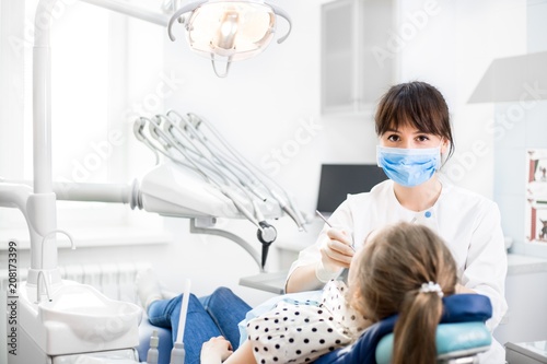 Dentist in uniform treats teeth patient sitting in a dental chair