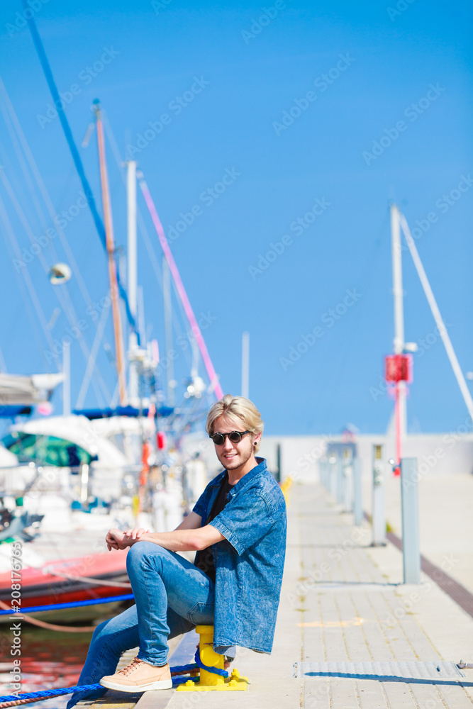 Blonde man sitting near harbor in summer