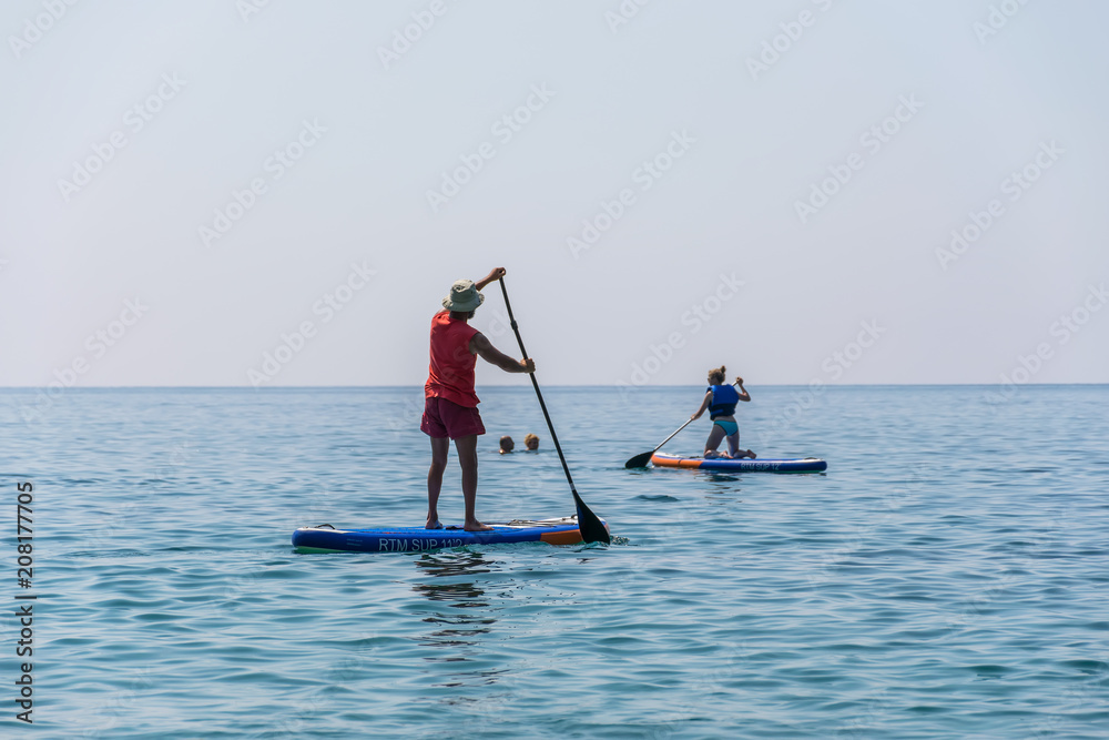 Naklejka premium MONTENEGRO, BUDVA - JUNE 05/2017: tourists are engaged in rowing on the board (SUP) on the surface of the calm sea.