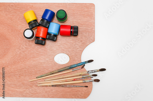 wooden art palette with paint and brushes isolated on white background, top view