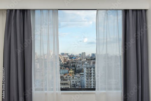 Beautiful view from the bedroom with window curtains and cityscape, blue sky, modern home decor.