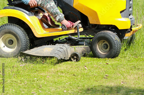 Gardener drive cutting grass with lawn mower.