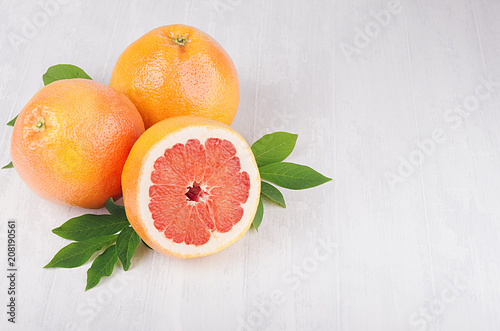 Whole and half slice grapefruits with green leaves on soft white wood background with copy space, top view.