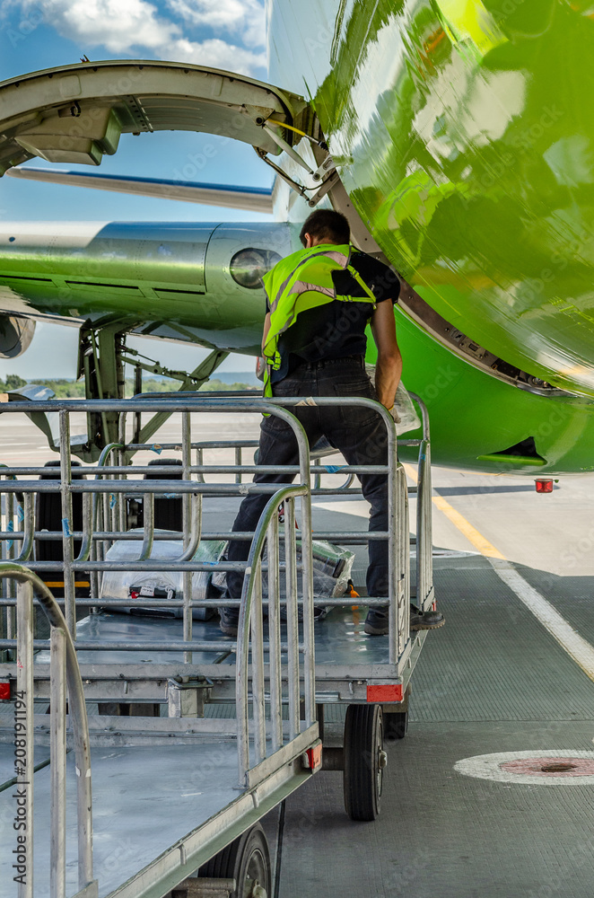 the process of unloading Luggage at the airport: suitcases taken out of the Luggage compartment of the aircraft and placed in the Luggage cart, green plane and blue sky