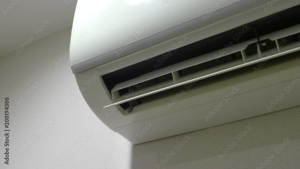 Air Conditioner on the wall is working which wind blade moving and swinging to provide cool wind to hot empty room but it may cause of global warming in the future.