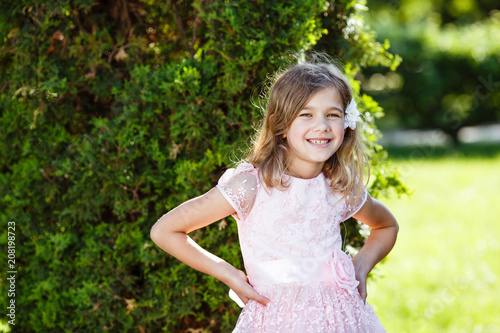 Portrait of a cheerful girl in a lush pink dress in the park.