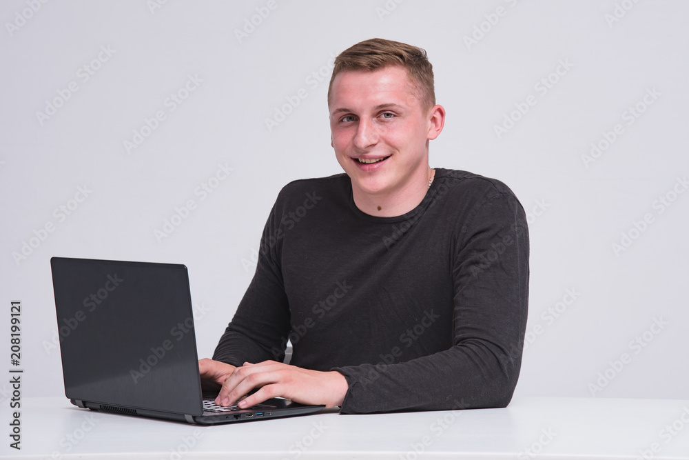 Portrait of a cute young guy with a laptop on a white background sitting at a table. Portrait of a cute young guy with a laptop on a white background sitting at a table.