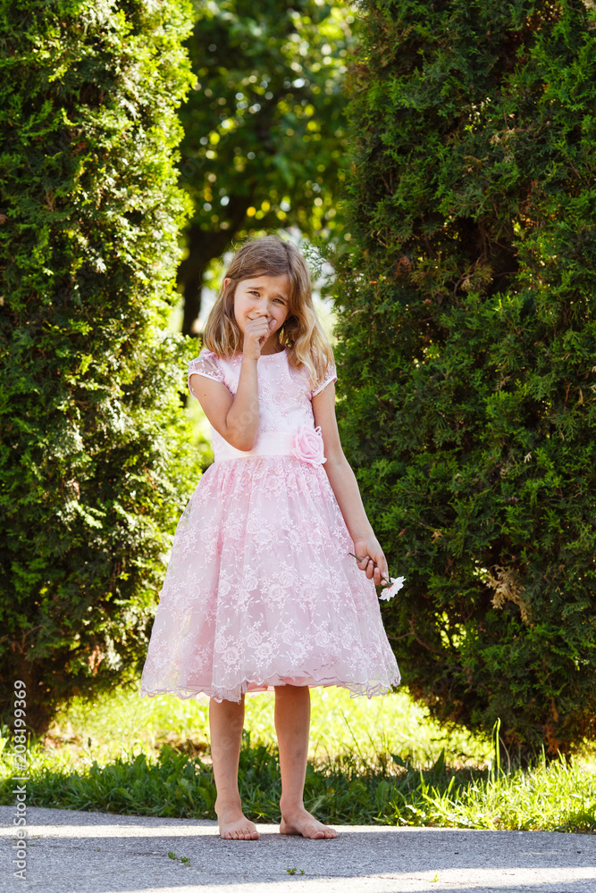 Portrait of a sad girl in a lush pink dress in the park.