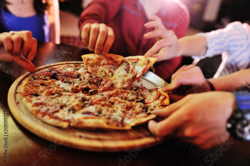 Photo Hands taking pizza slices from wooden plate