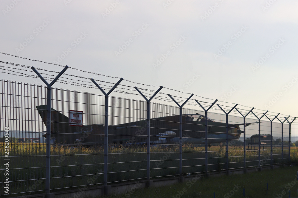 Military aircraft fighter at a grassy airfield. High technologies of the military industry. Romance of military specialty. The enclosed territory is surrounded by a metal fence with a barbed wire. Military aircraft fighter at a grassy airfield. High technologies of the military industry. Romance of military specialty. The enclosed territory is surrounded by a metal fence with a barbed wire.
