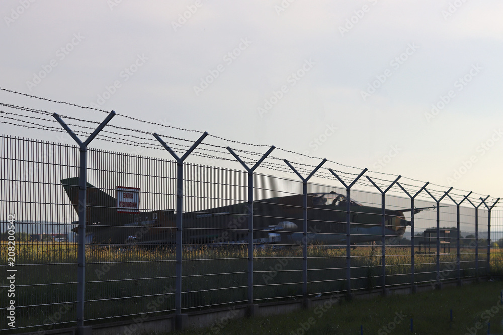 Military aircraft fighter at a grassy airfield. High technologies of the military industry. Romance of military specialty. The enclosed territory is surrounded by a metal fence with a barbed wire.