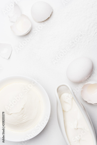 top view of sour cream and cracked egg shells on white surface spilled with flour