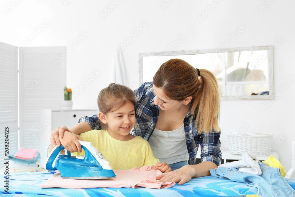 Fototapeta premium Housewife with daughter ironing clothes in laundry room