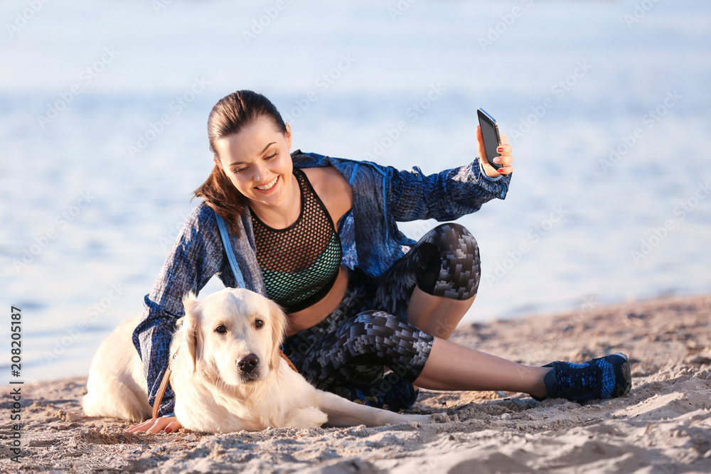 Young woman taking selfie with together her dog on beach. Pet care