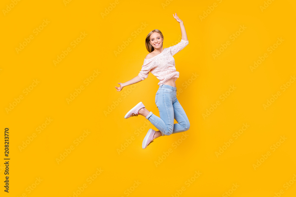 Portrait of playful crazy girl jumping in the air looking at camera enjoying weekend having perfect mood isolated on yellow background