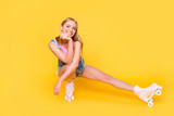 Portrait of cheerful charming girl sitting on roller skates making break time out pause looking at camera isolated on yellow background