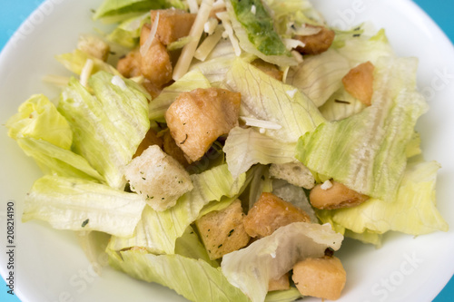 Appetizing salad of fresh vegetables, chicken pieces, toast and cheese in a white plate on a blue background close-up