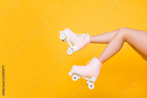 Cropped portrait of legs in pink vintage quad roller skates shoes isolated on yellow background, extreme balance concept, street outside urban lifestyle style, laser hair removal perfect skin photo