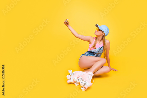 Portrait with copy space empty place for advertisement, lovely girl shooting self portrait on front camera using smart phone sending blowing kiss having booty ass bum isolated on yellow background