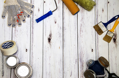 top view, a set of tools for painting, mask to protect from harmful air, brushes, rollers, cans of paint,goggles and gloves for hands on a white wooden background