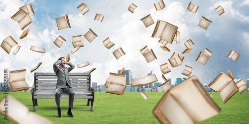 Many old books falling from above and student guy sitting on bench