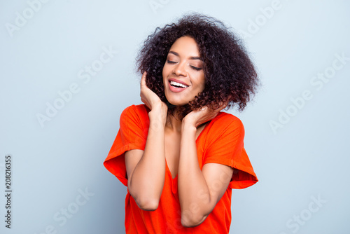 Portrait of cheerful funky woman with modern hairdo in bright t-shirt touching hair keeping eyes closed having beaming smile isolated on grey background © deagreez