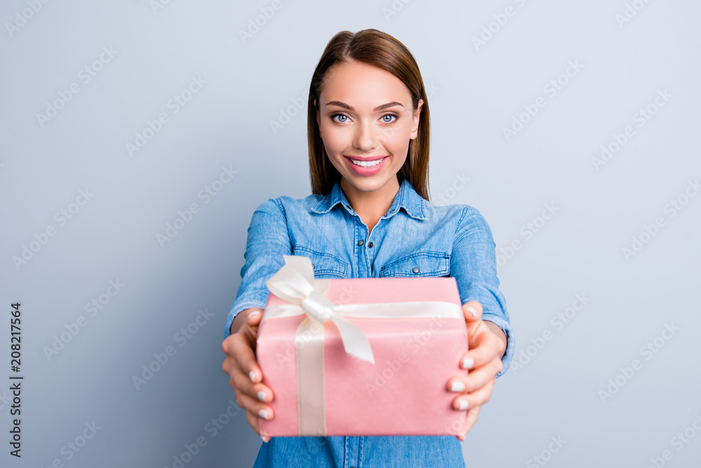 Portrait of cute charming girl presenting a gift in pink packaging with white bow standing over grey background Portrait of cute charming girl presenting a gift in pink packaging with white bow standing over grey background