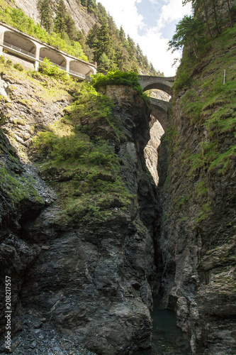 Lateral view of the canyon in the Alps of Switzerland. Above you can see a part of the car path and a bridge over the gorge. Between the rocks flows a river called Rhine.