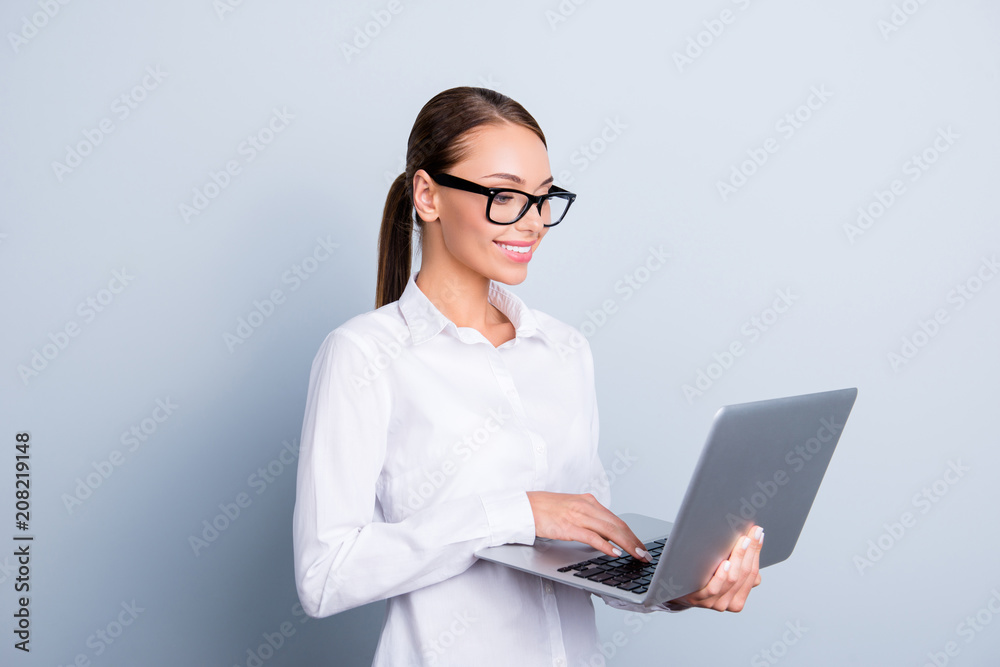 Half-turned portrait of elegant clever woman with ponytail toothy beaming smile charming agent using netbook isolated on grey background Half-turned portrait of elegant clever woman with ponytail toothy beaming smile charming agent using netbook isolated on grey background