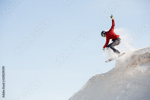 Photo of man in helmet with snowboard jumping from snowy mountain slope