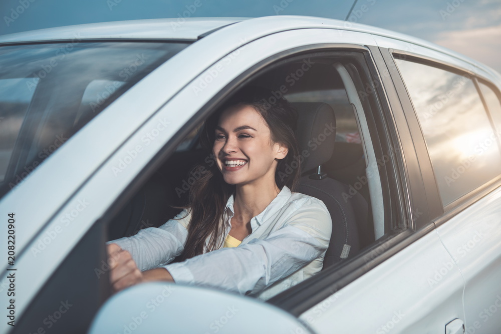 Joyful girl is driving a car with excitement. She is sitting steering wheel and smiling Joyful girl is driving a car with excitement. She is sitting steering wheel and smiling