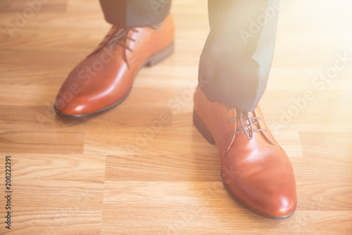 Body detail of businessman. Sunlight bokeh. Man wearing shoes on wooden floor. Clothing concept, groom getting ready before ceremony.