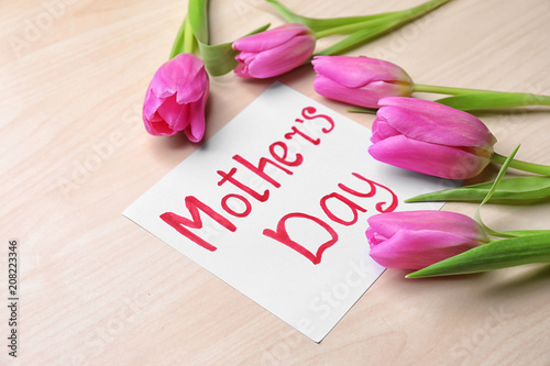 Beautiful tulips and card for Mother's Day on light wooden background