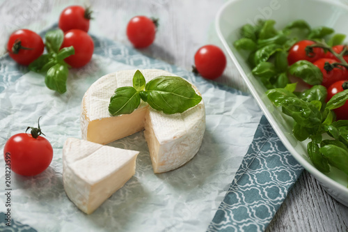 Delicious brie cheese with basil and cherry tomatoes on table