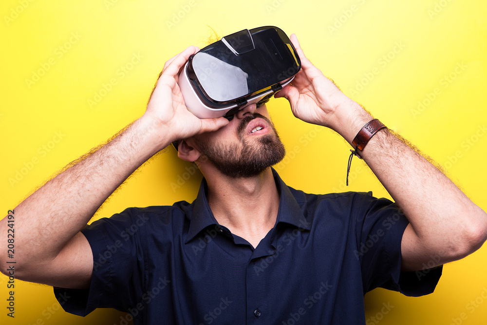 Young man wearing a Virtual Reality headset on yellow background in studio Young man wearing a Virtual Reality headset on yellow background in studio