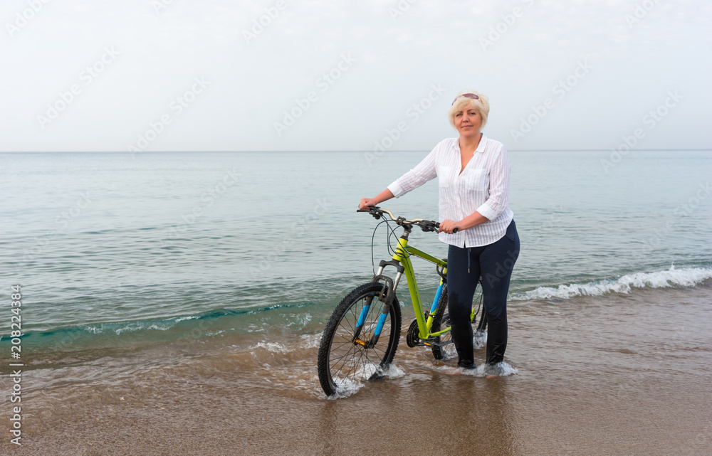 Fototapeta premium Woman wheeling her bicycle through the sea