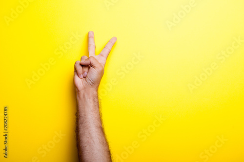 Male hands showing victory sign over yellow background in studio photo