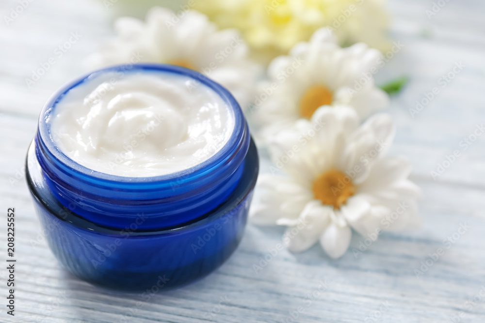 Jar with cream and flowers on wooden background. Skin care cosmetics