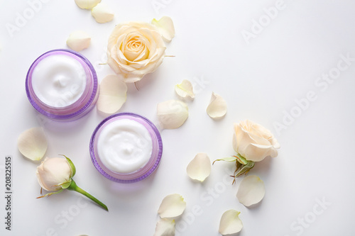 Jars with skin care cosmetics and flowers on white background