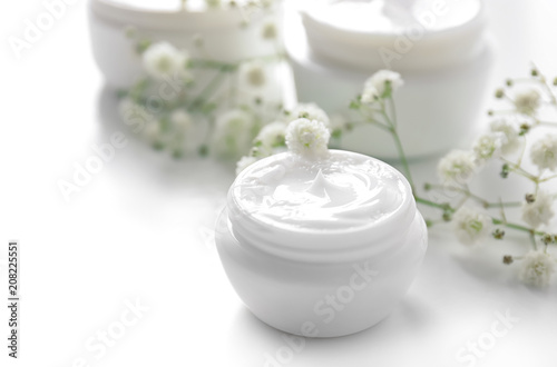 Jar with cream and flowers on white background. Skin care cosmetics