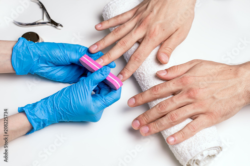 Men's manicure. Cosmetologist in rubber gloves file nails on male hands.