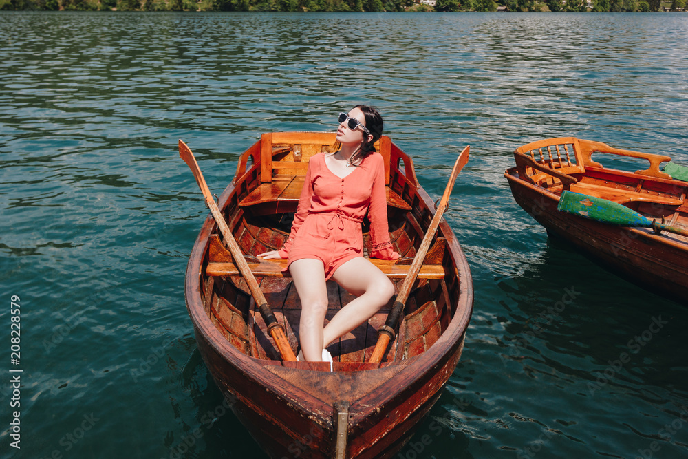 Obraz premium beautiful girl in sunglasses sitting on wooden boat on lake